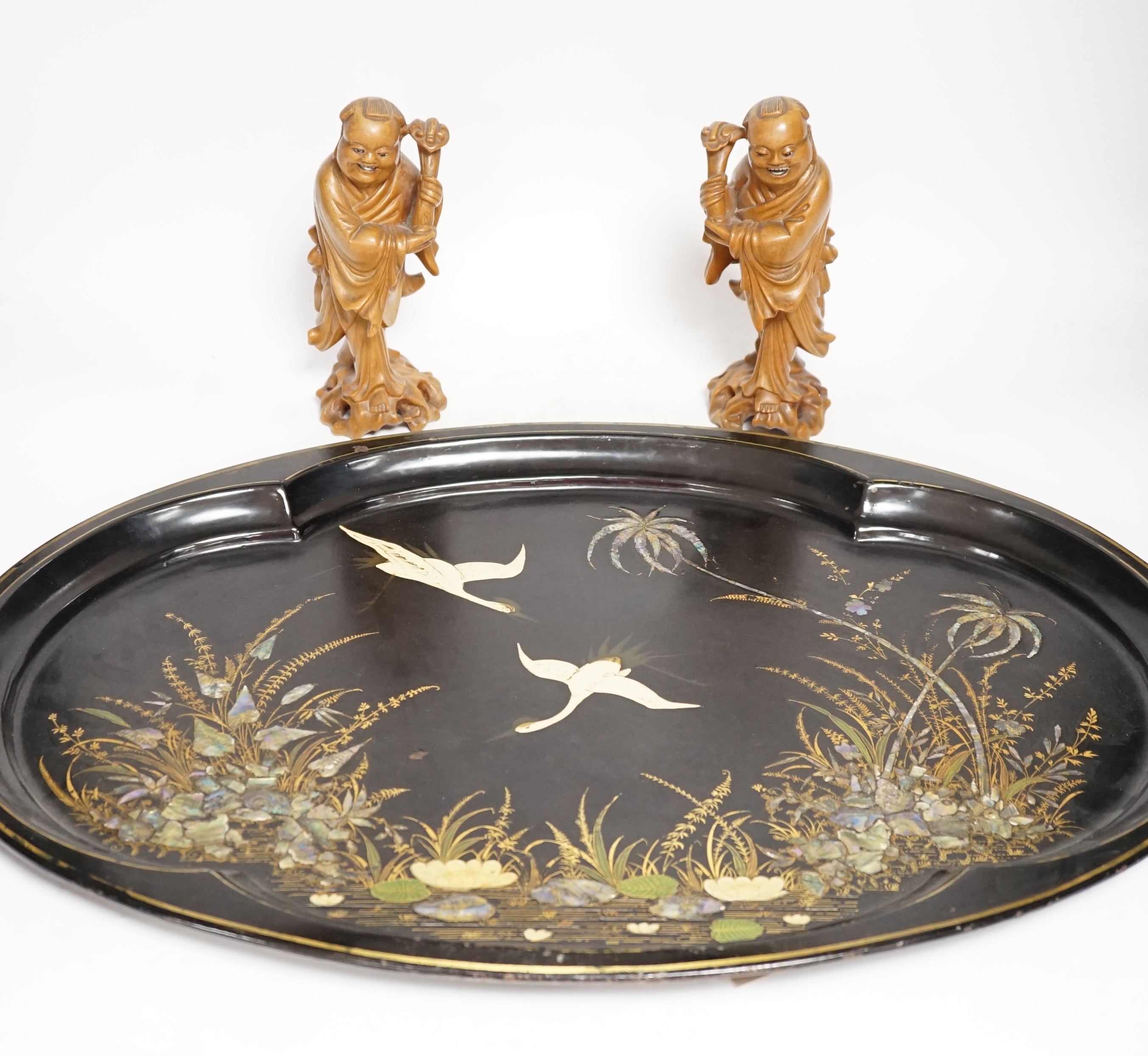 An oval japanned toleware tray and a pair of Chinese carved wood figures, largest 61cm wide